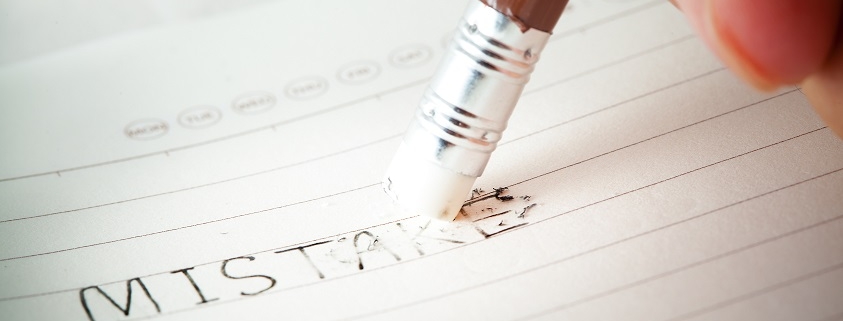 Hand erasing the word mistakes on a sheet of lined paper