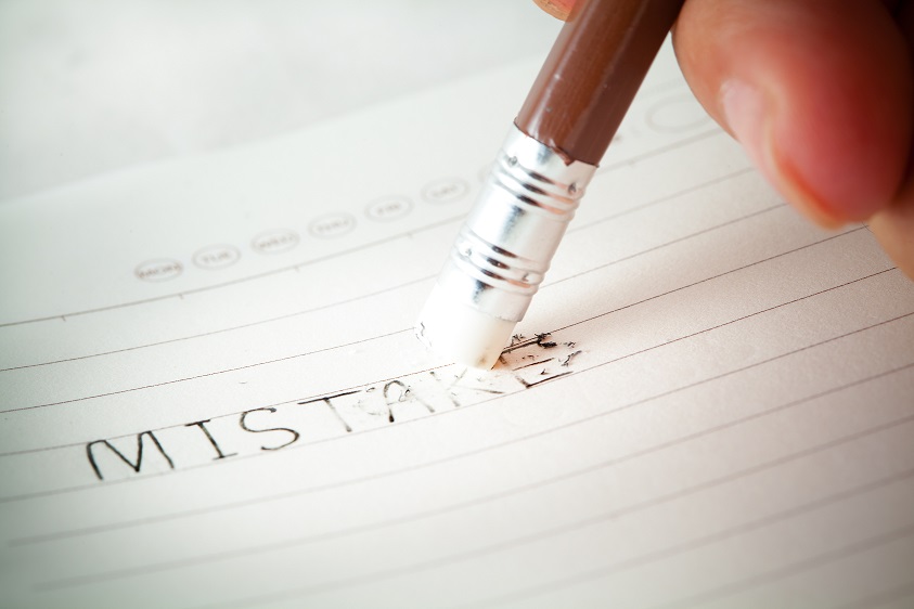 Hand erasing the word mistakes on a sheet of lined paper